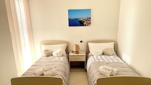 A twin bedroom with two beds, a nightstand, a lamp, and a framed picture on the wall. - Luxury Apartments  (Polignano a Mare)