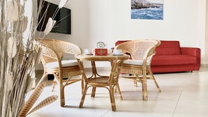 A room with a wicker table and chairs, a red sofa, a flat-screen TV, and a coastal cityscape poster. - Luxury Apartments  (Polignano a Mare)