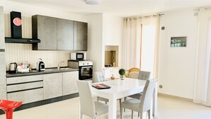 A modern kitchen with a microwave, oven, and a clock on the wall. There is a dining table with chairs and a red bar stool. - Luxury Apartments  (Polignano a Mare)
