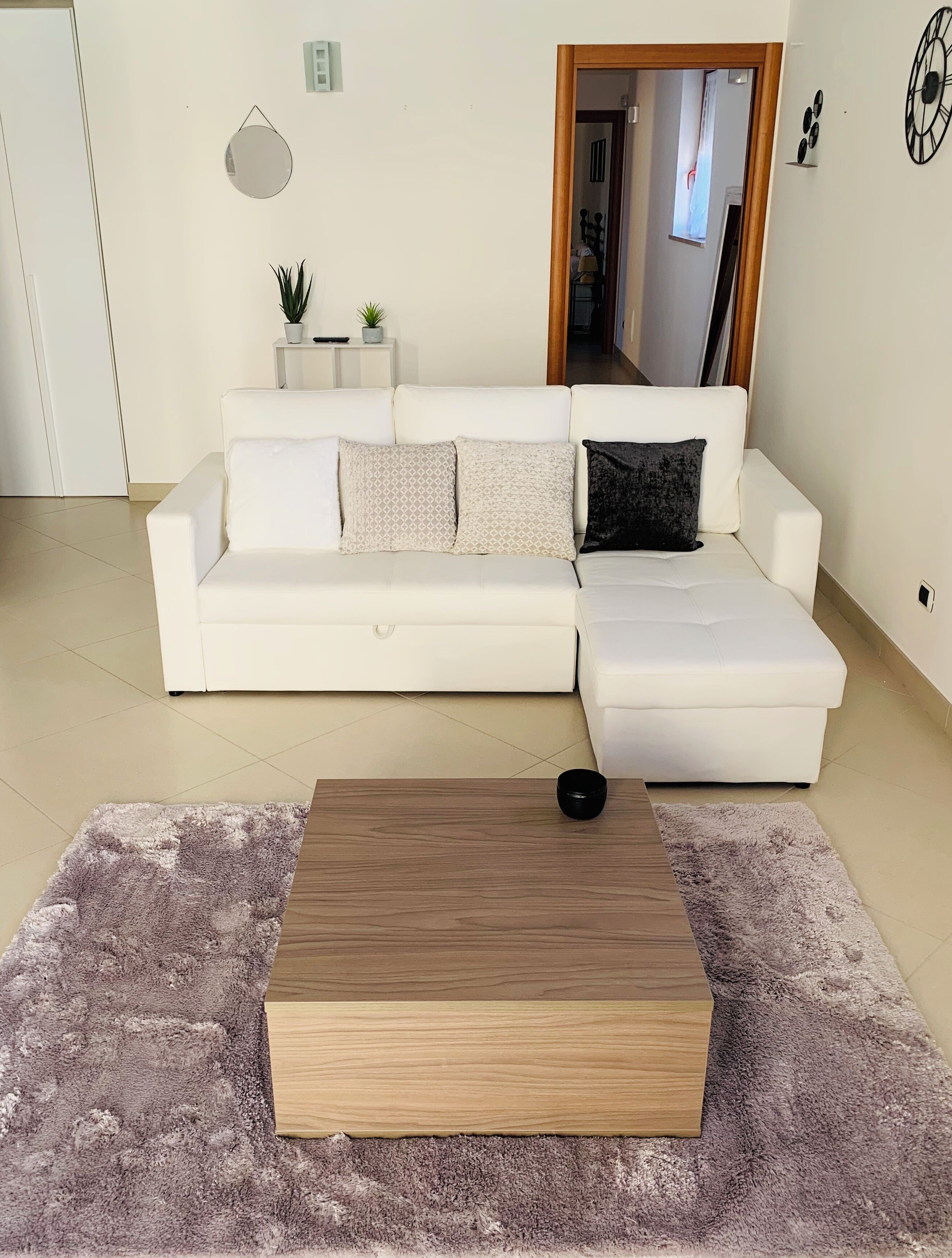 Una sala de estar moderna con un sofá seccional blanco, una mesa de centro de madera y una alfombra mullida.