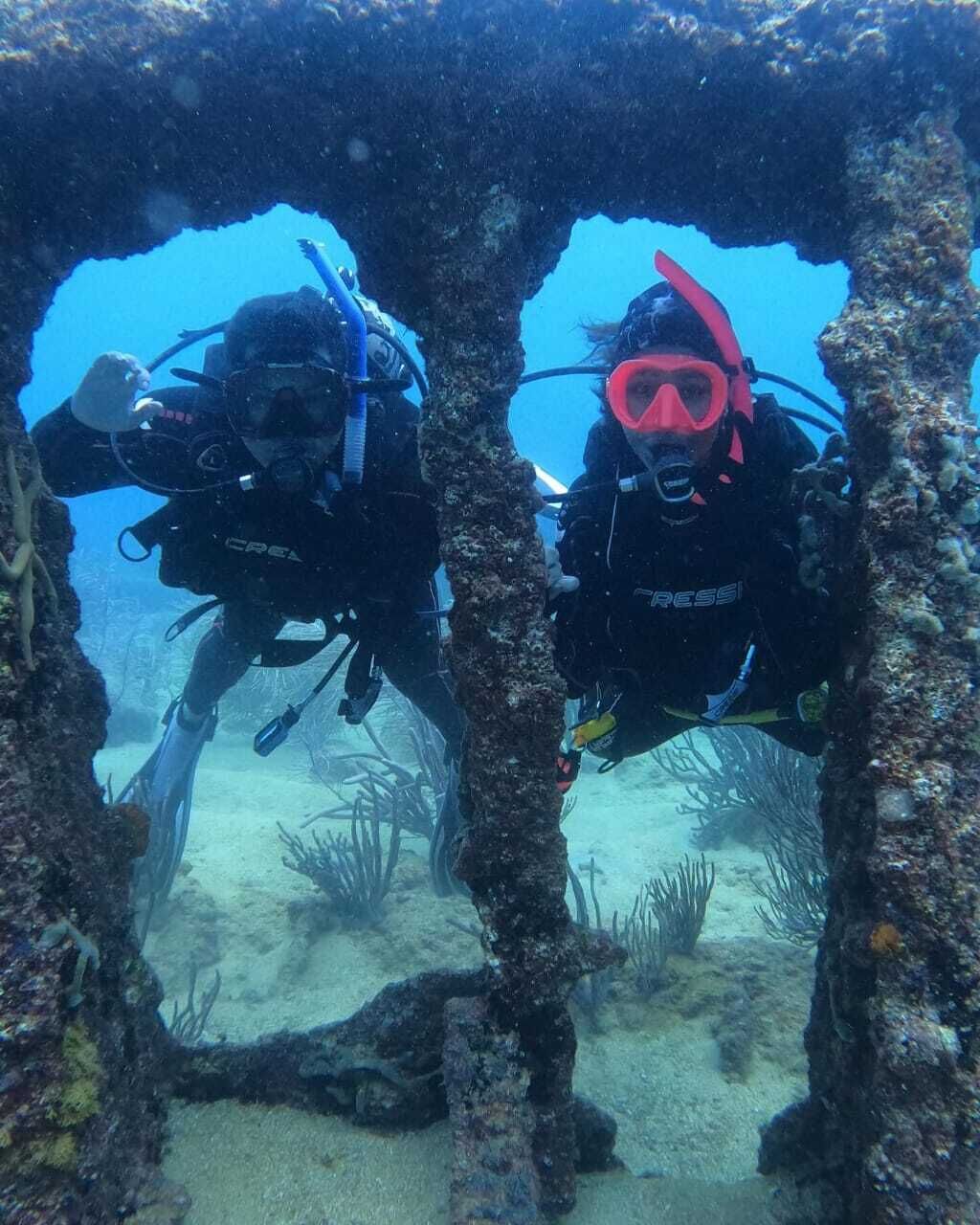 Two divers exploring an underwater cave with visible coral formations and marine life.