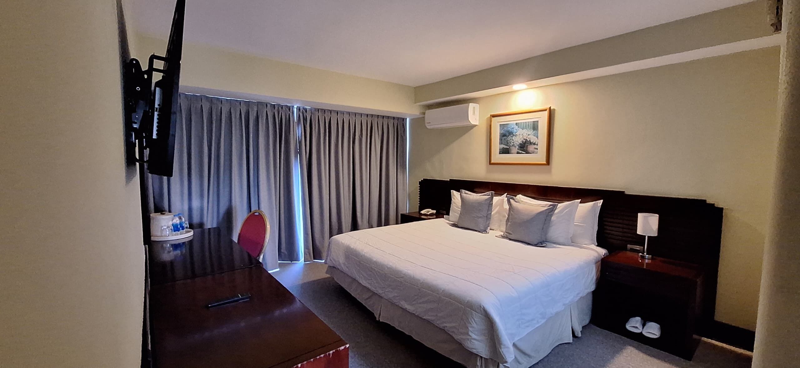 Ein Hotelzimmer mit Bett, Nachttisch, Lampe und einem an der Wand montierten Fernseher.