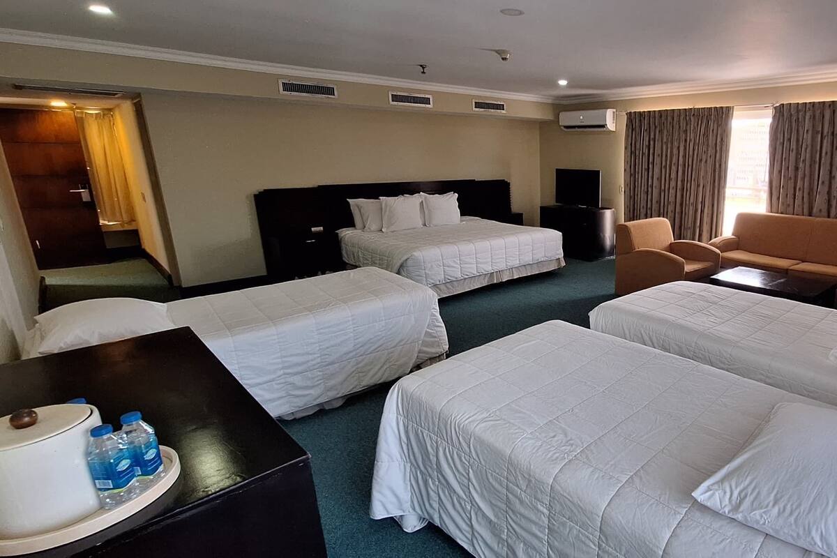 A hotel room with two single beds, a sofa, a small table, and a TV.