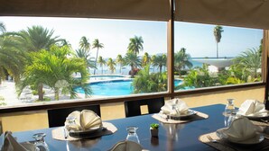 Mesa de comedor preparada para cuatro personas, con vistas a una piscina y palmeras.