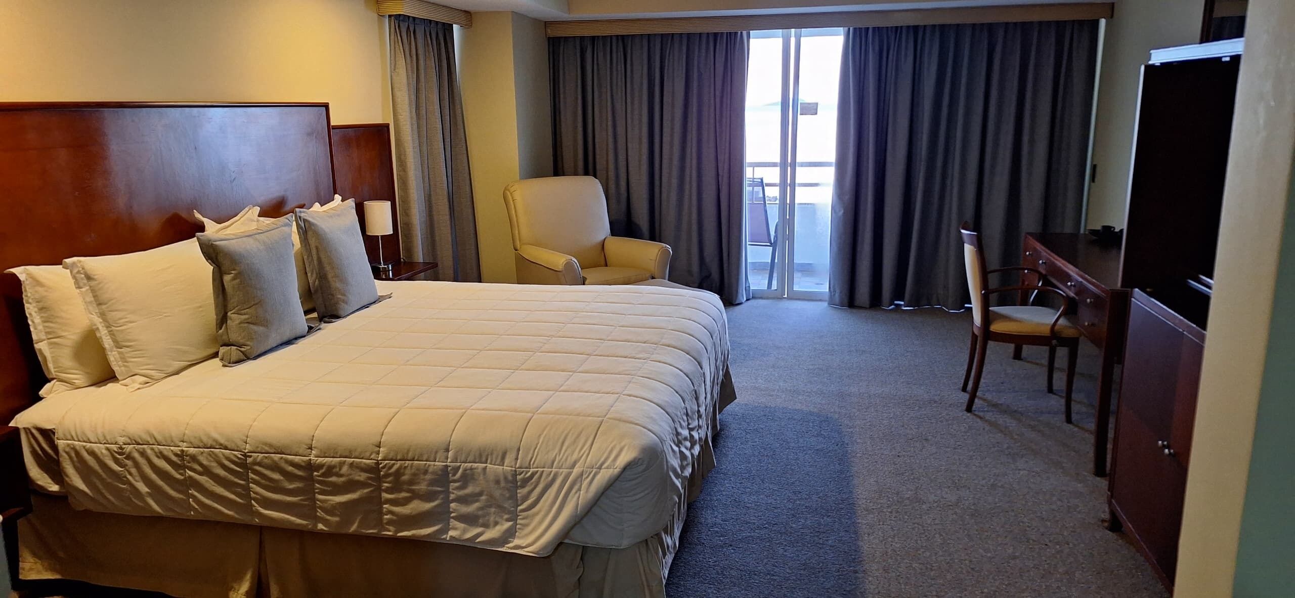 A hotel room with a large bed, a desk, a chair, and a television.