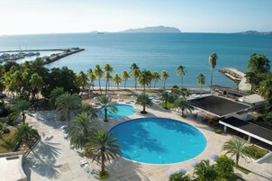 Um resort com uma piscina grande, palmeiras e vista para o oceano.