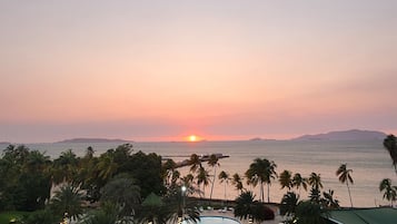 Une piscine d’hôtel offrant une vue sur le coucher du soleil, entourée de palmiers et de chaises longues.