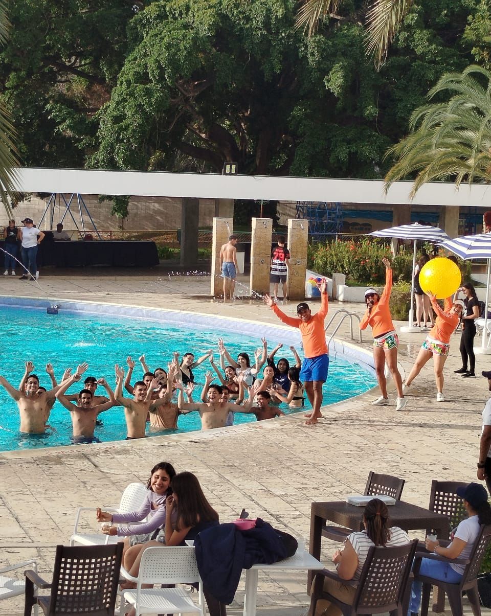 A poolside area with people around a pool, some standing and others seated.