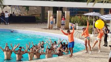 A poolside area with people around a pool, some standing and others seated.