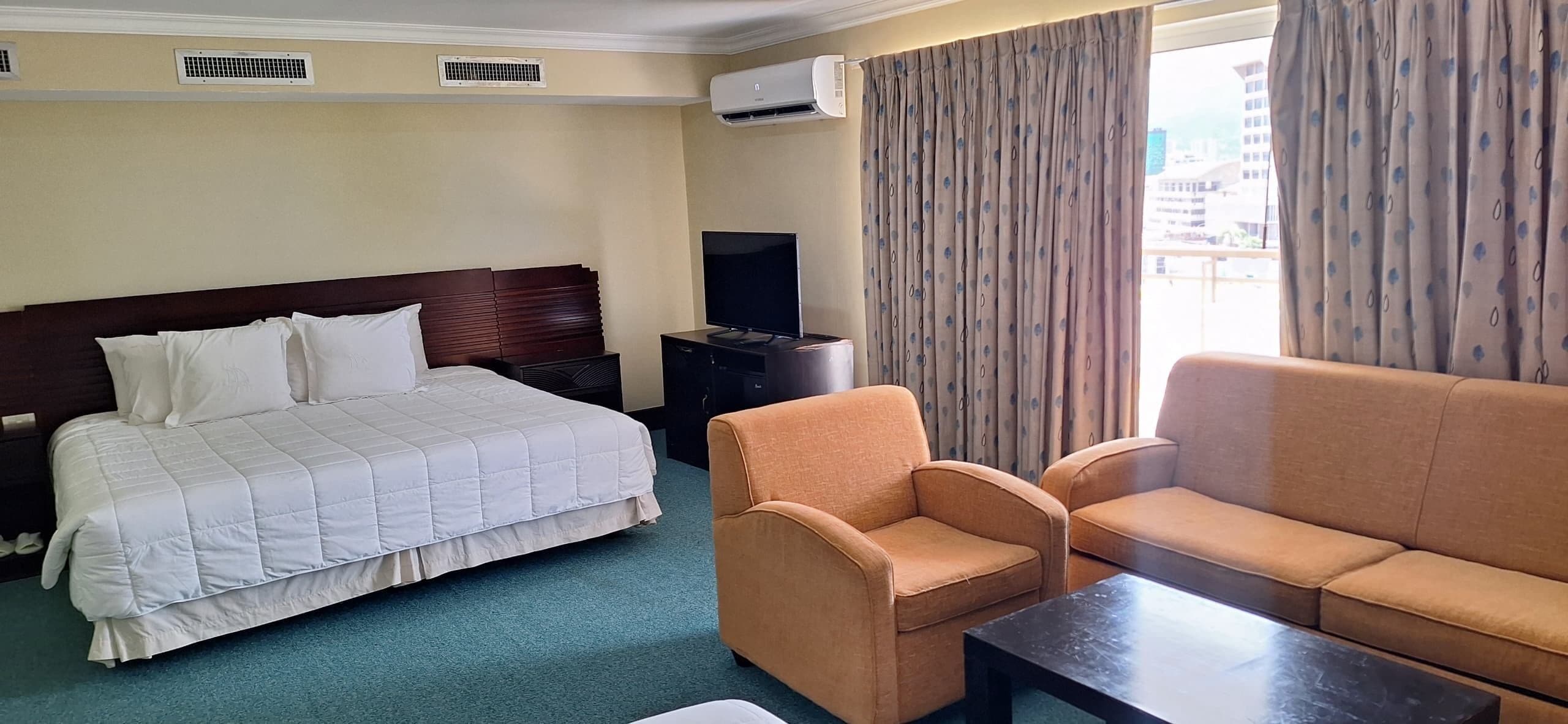 Une chambre d’hôtel avec un lit, une télévision, un canapé et une fenêtre avec des rideaux.