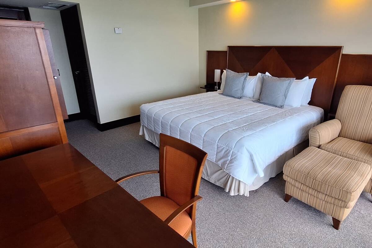 A hotel room with a bed, a wooden desk, a chair, and a wardrobe.