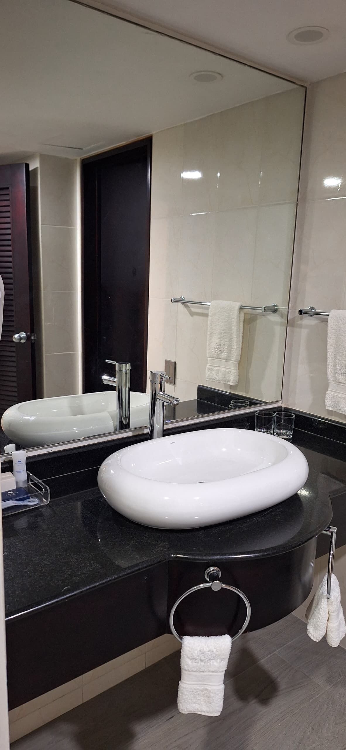 Une salle de bain moderne avec un grand miroir, deux lavabos, un porte-serviettes et une cabine de douche en verre.