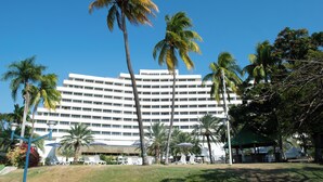 Un hotel grande con varios pisos, rodeado de palmeras y un césped cuidado.
