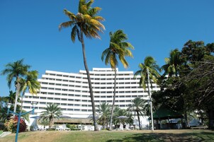 Um hotel grande com vários andares, rodeado por palmeiras e um gramado bem cuidado.