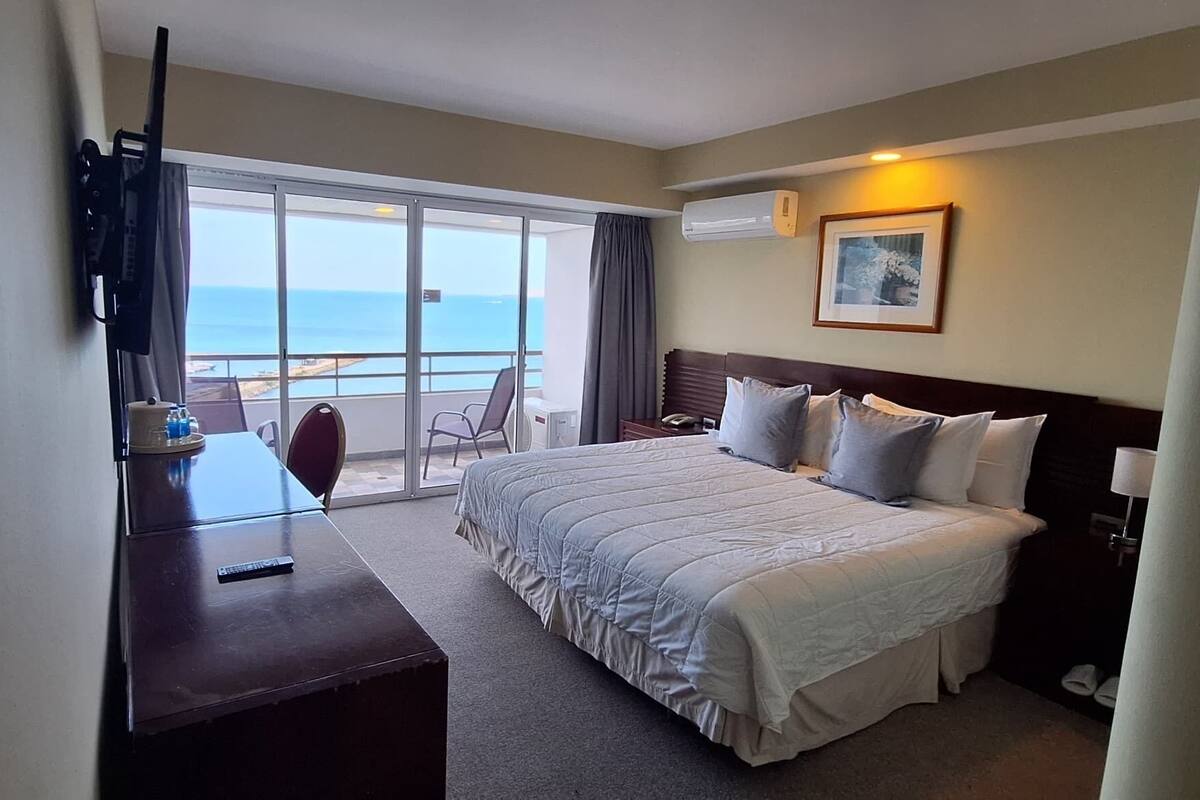 A hotel room with a bed, a desk, a chair, and a view of the ocean.