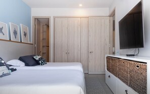 Un dormitorio con cama, televisor, armario y una pared con cuadros.