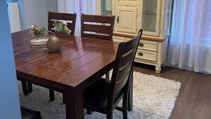 Un comedor con una mesa de madera, cuatro sillas, una araña y un aparador con puertas de cristal.