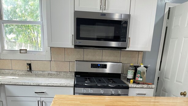 Una cocina con armarios blancos, encimera de madera, estufa de acero inoxidable y un microondas.