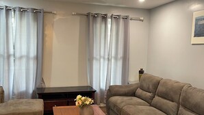 Una sala de estar con un sofá, una mesa de centro de madera con un florero, un pequeño reposapiés y una mesita auxiliar de madera oscura.