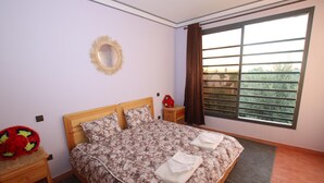 Une chambre à coucher avec un lit, une table de chevet, un miroir et une fenêtre avec des rideaux.