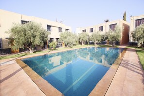 A rectangular pool with clear blue water, surrounded by a paved area and trees. - Very beautiful guesthouse to rent (Marrakech)