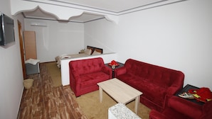 Un espace de vie compact comprenant un canapé rouge, une petite table et un téléviseur fixé au mur.