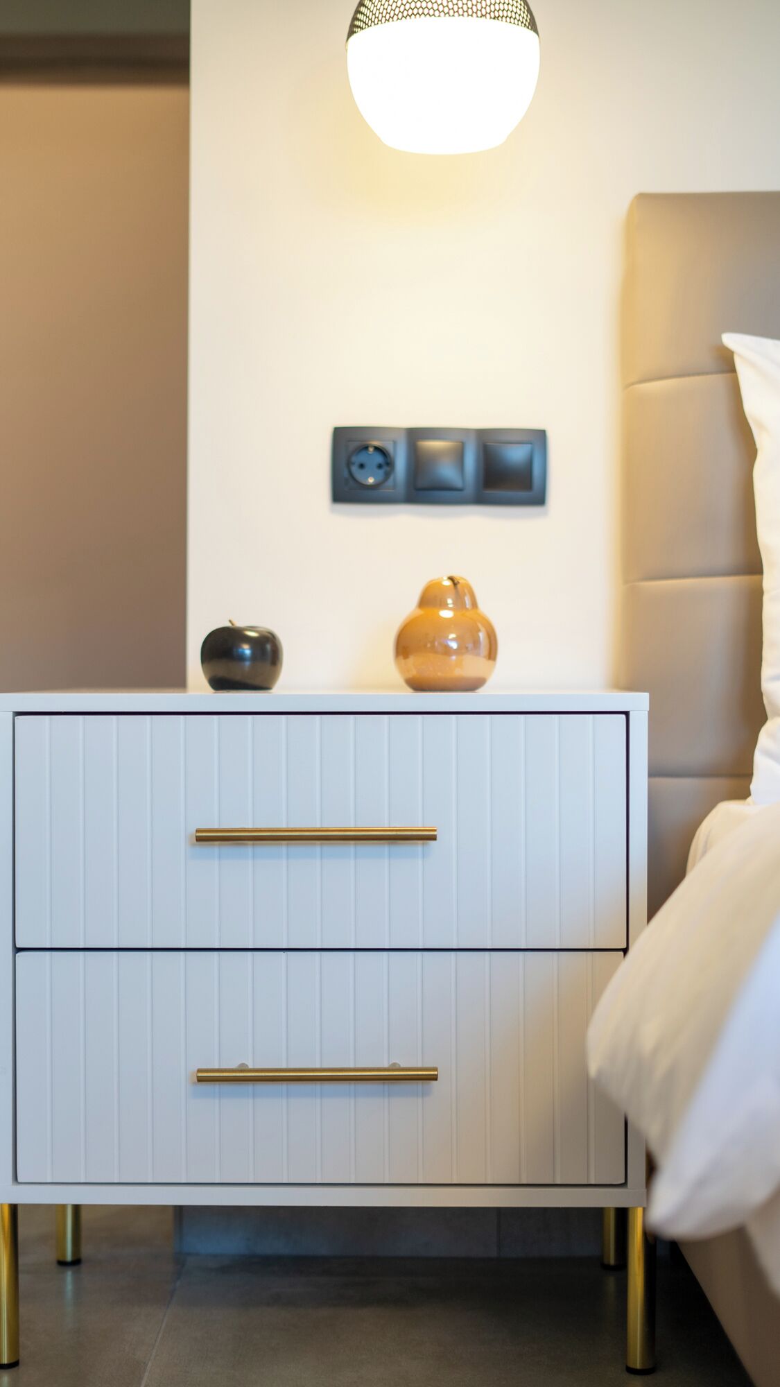 A modern bedroom with a white nightstand, a wall-mounted light fixture, and a small decorative item.