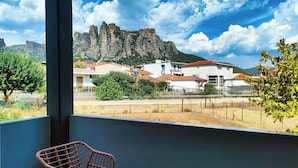 A balcony with wicker chairs, a small table, and a view of buildings and rocky mountains.