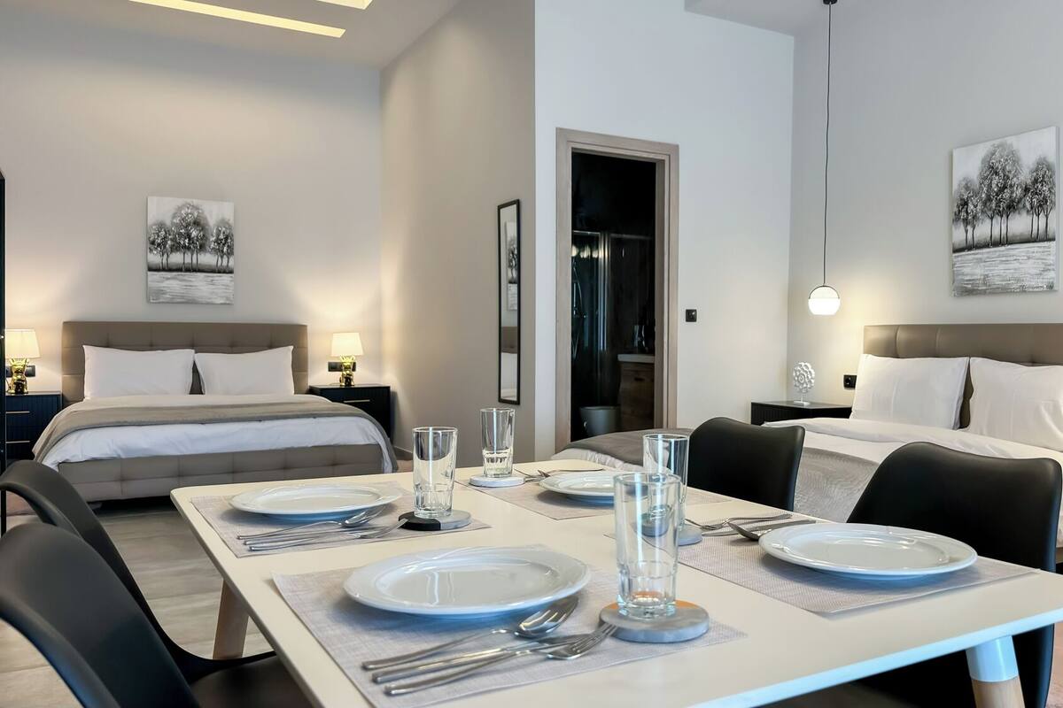 Een moderne hotelkamer met twee bedden, een eettafel gedekt voor twee personen, en kunstwerken aan de muur.