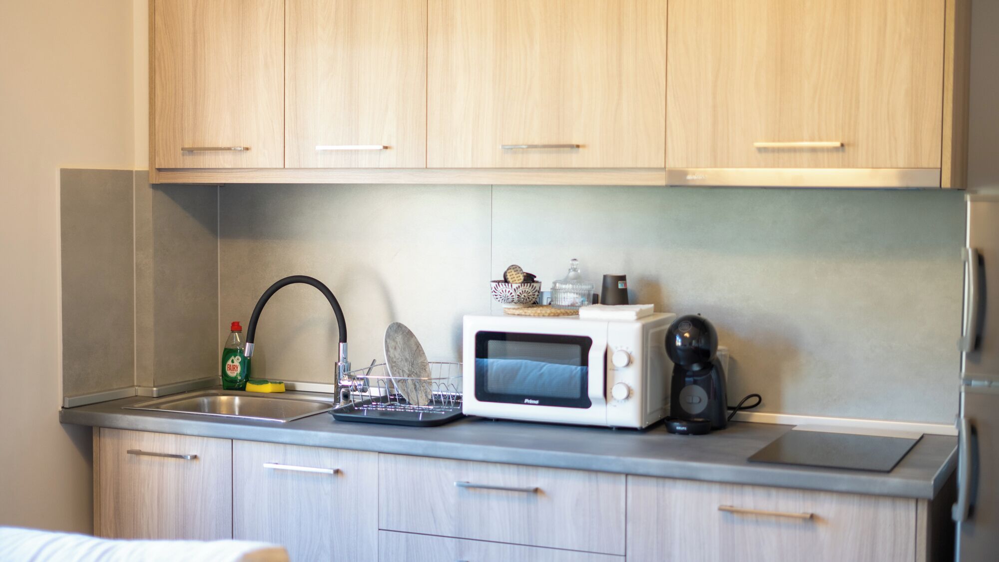 A kitchen with wooden cabinets, a stainless steel sink, a microwave, and a kettle.
