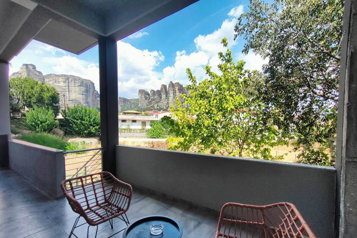 Een balkon met rieten stoelen en een tafeltje, met uitzicht op een landschap met bomen en gebouwen.