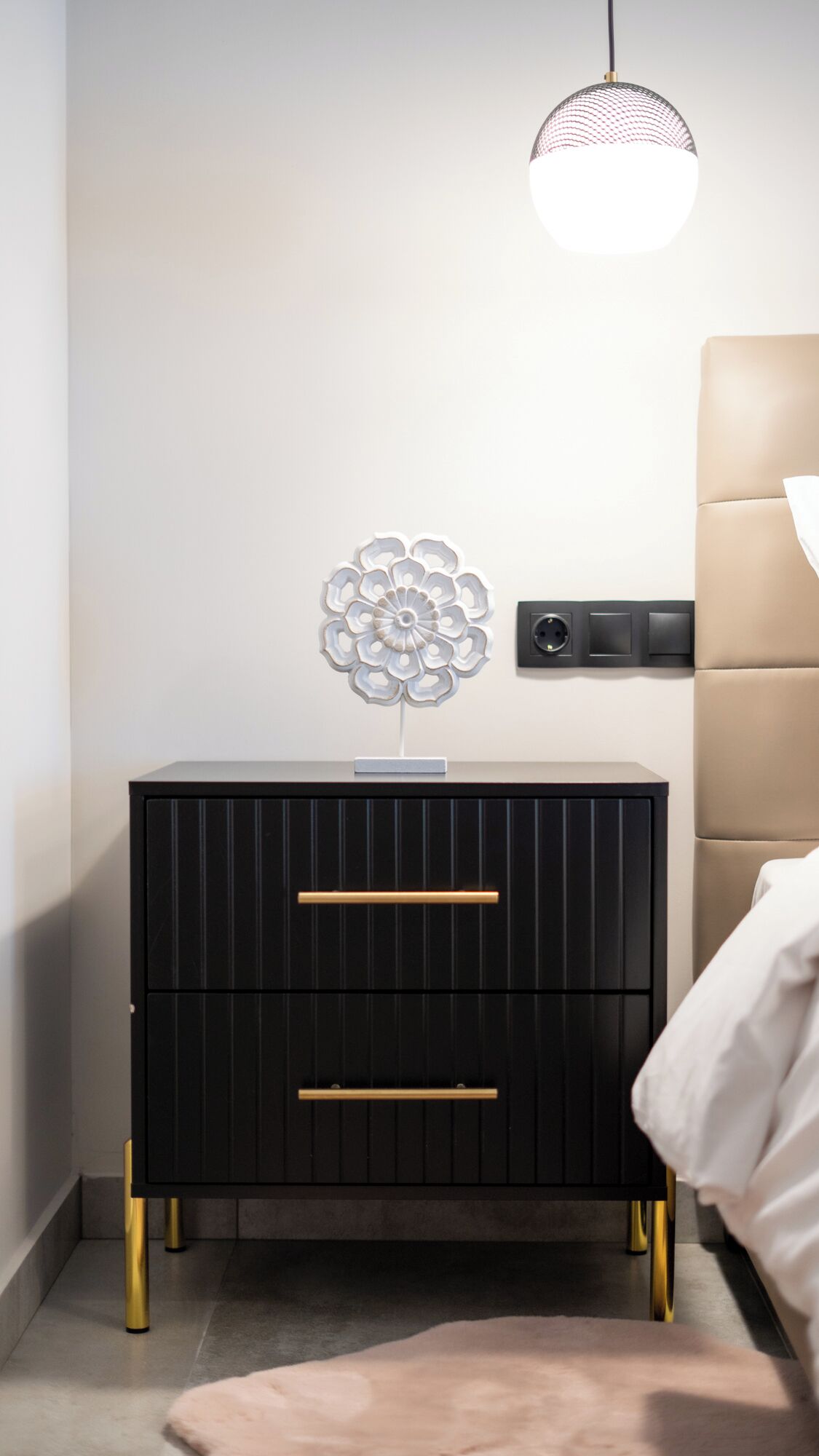 A black nightstand with gold handles, a decorative wall piece, and a bedside lamp.