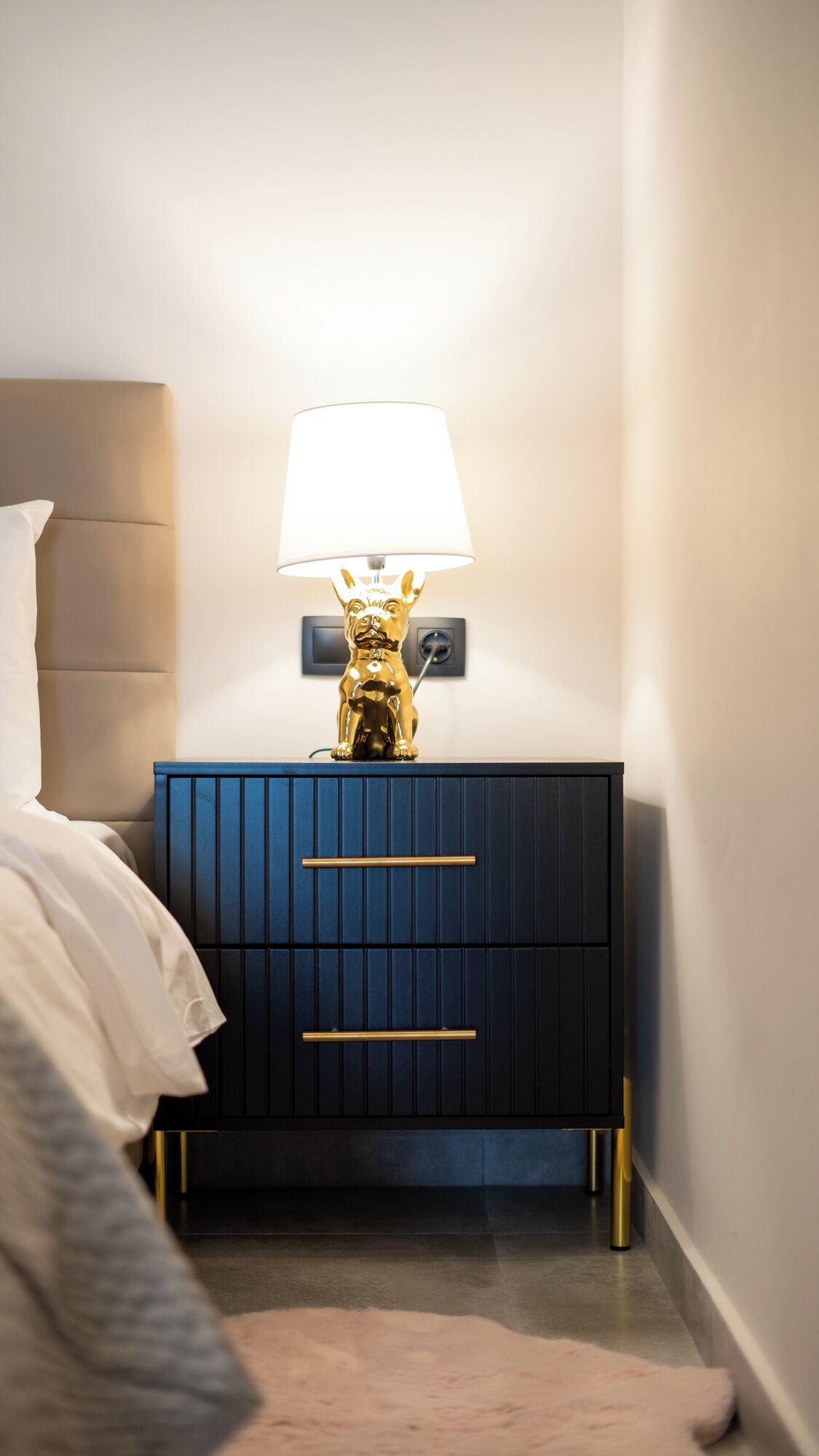 A modern bedroom with a bed, a nightstand with a lamp, and a decorative dog statue.