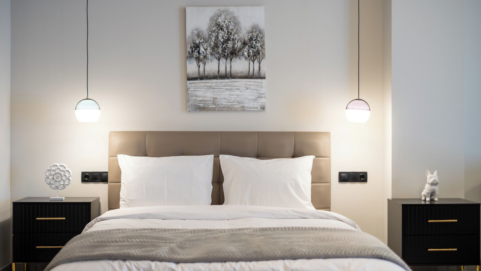 A bedroom with a large bed, two bedside tables, a wall-mounted artwork, and pendant lights.