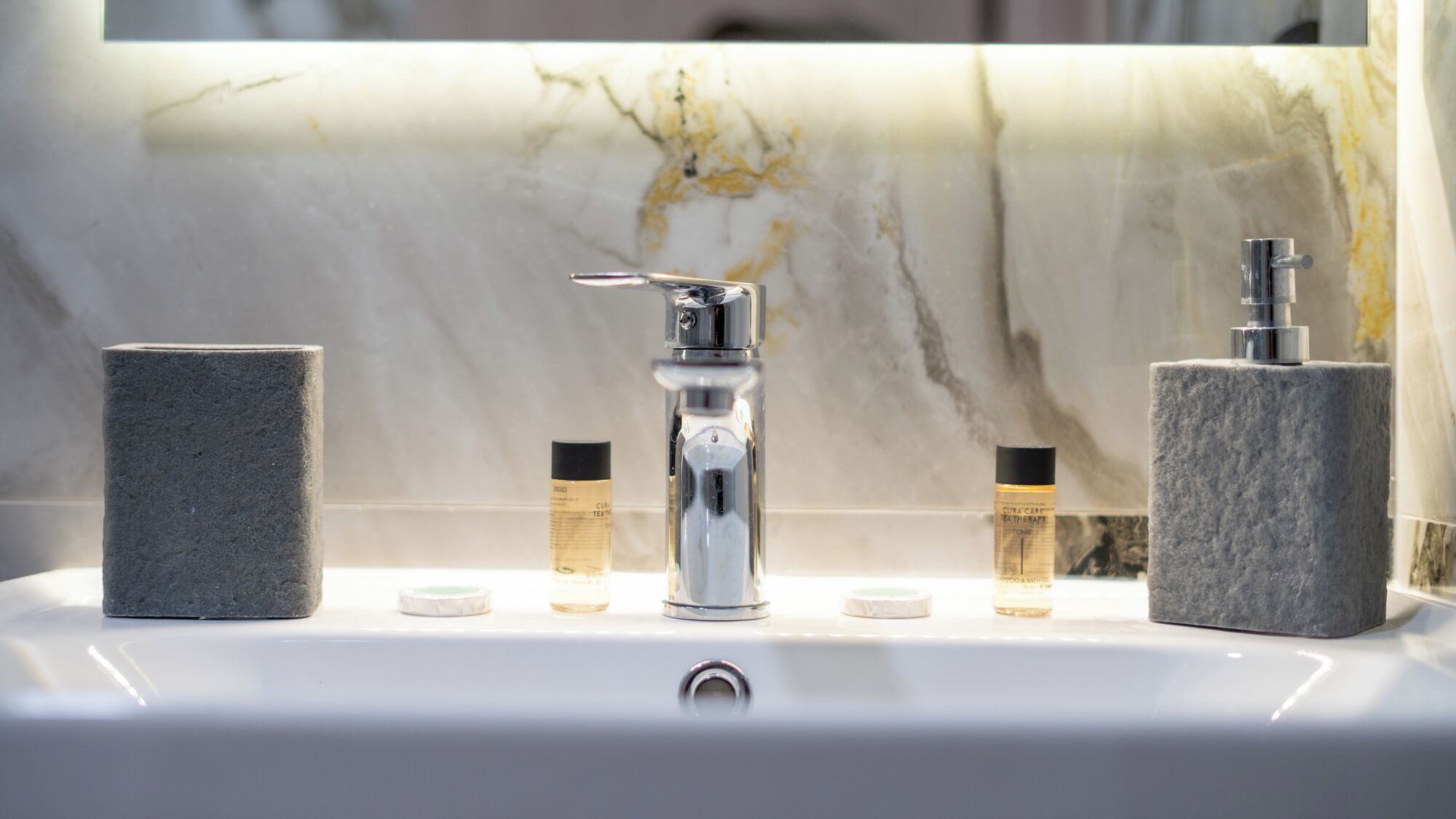 Un lavamanos de baño con un grifo moderno, dos dispensadores de jabón y dos pastillas de jabón que parecen piedra.