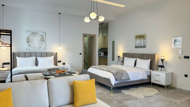 A modern hotel room with two beds, a sofa, a dining table with breakfast items, and artwork on the walls.