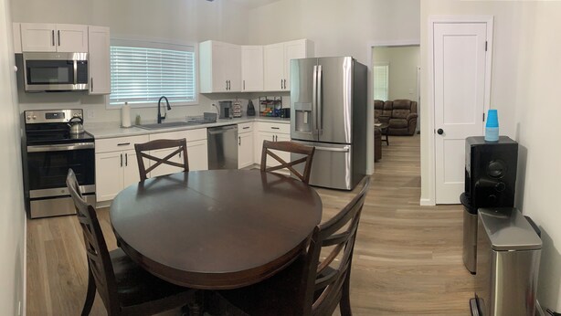 A modern kitchen with white cabinets, stainless steel appliances, a round wooden dining table, and a compact living area with a sofa and a door leading to another room. - Newly Remodeled 3-BR in heart of Marion (Marion)