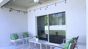 An outdoor patio with white furniture, green cushions, and string lights. - Beach home 3br 2ba in Palm Coast (Palm Coast)