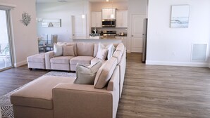 A spacious living area with a large beige sectional sofa, a glass dining table, and a kitchen with white cabinets and stainless steel appliances. - Beach home 3br 2ba in Palm Coast (Palm Coast)