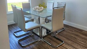 A dining area with a glass table, white chairs, a chandelier, and a painting on the wall. - Beach home 3br 2ba in Palm Coast (Palm Coast)