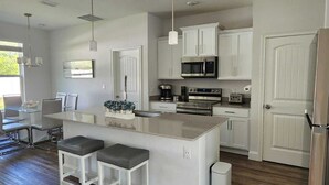 A modern kitchen with white cabinetry, stainless steel appliances, and a central island with bar stools. - Beach home 3br 2ba in Palm Coast (Palm Coast)