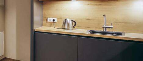 A modern kitchen with a stainless steel kettle, a sink, and wooden cabinets.