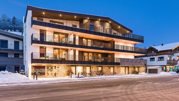 A multi-story hotel with balconies, a stone facade, and a snow-covered ground. - Apartment Brixen im Thale (Brixen im Thale)