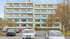 Een meerlaags woongebouw met een parkeerplaats ervoor.