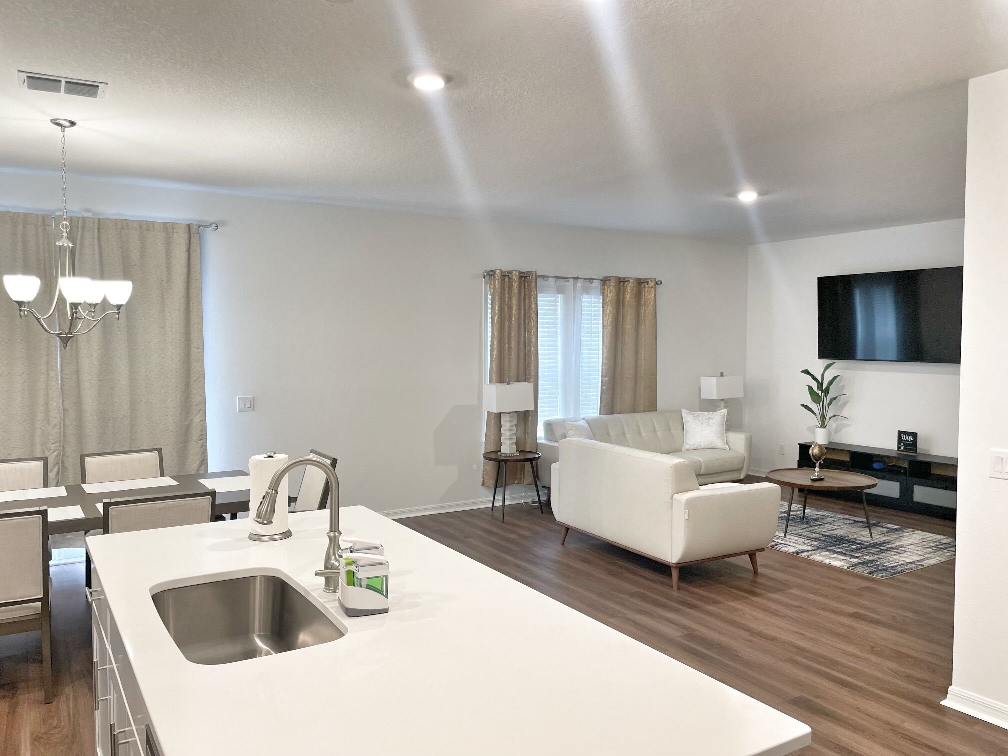 Una cocina moderna con una isla central, un comedor con sillas, una sala de estar con sofá y un televisor montado en la pared.