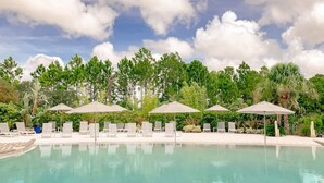 Ein Poolbereich mit Liegestühlen und Sonnenschirmen, umgeben von Bäumen und blauem Himmel.