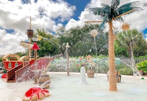Ein Wasserpark mit einem thematisch gestalteten Spielbereich im Schiffsstil, einer Palme und einer Fontäne.