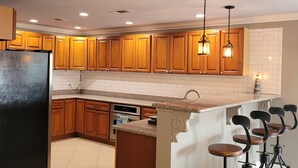 Una cocina con armarios de madera, un refrigerador negro, una isla integrada con taburetes y luminarias colgantes.
