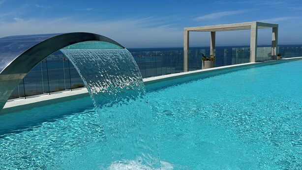 Une piscine d’un bleu éclatant, agrémentée d’une cascade, une balustrade en verre et une vue sur l’océan.