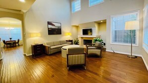 A spacious living room with hardwood flooring, a sofa, a coffee table, and a fireplace. There are two lamps, a TV mounted above the fireplace, and a painting on the wall. -  Luxury home in Newport Beach city Near UCI (Newport Beach)
